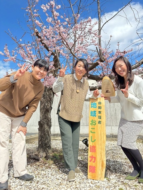 退任する地域おこし協力隊の3人が桜の前で記念撮影している写真